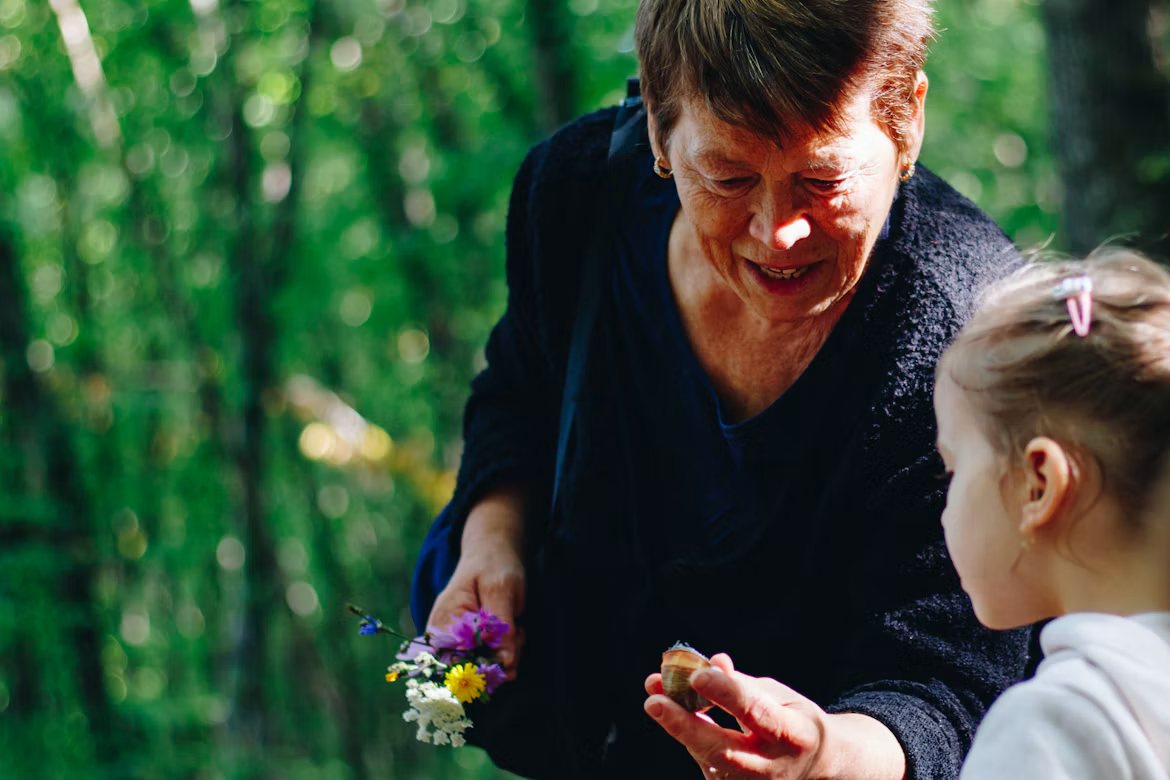 Bestemor viser et barn blomster i skogen